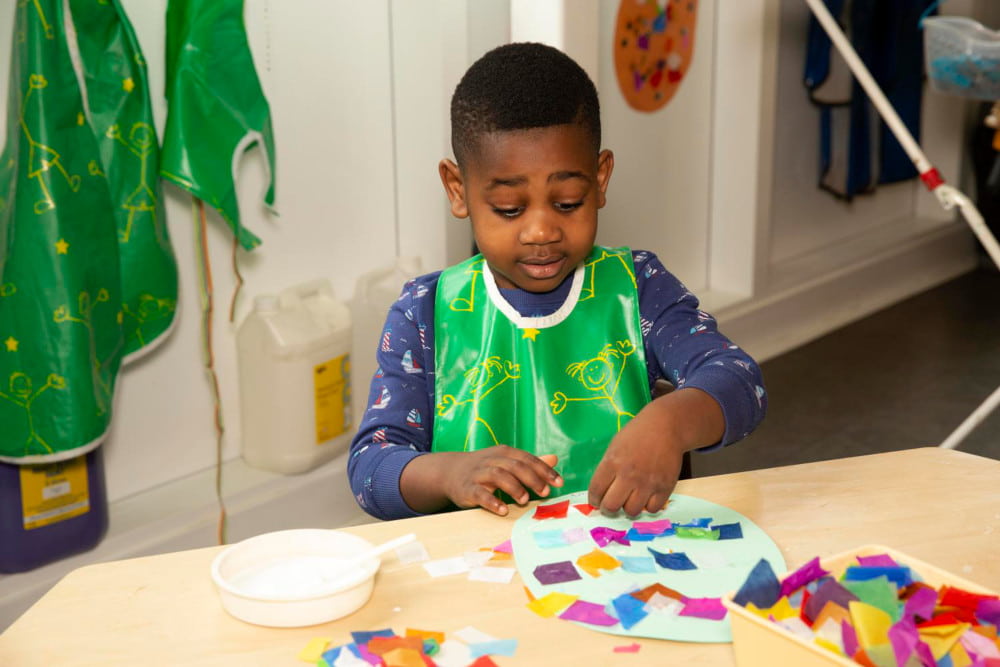 Image of a boy making a craft project at a table in a classroom.