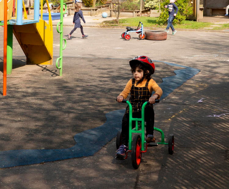 Image of a child riding a tricycle in a playground.