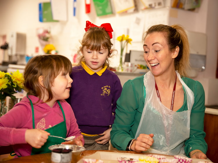 Image of an adult and two children sitting at a table and smiling at each other in a playroom.