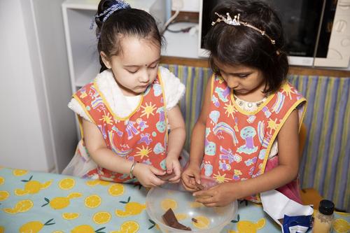 Image of two children breaking up pieces of chocolate in a bowl at a table in a playroom.