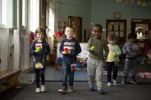 Image of children smiling and walking towards the camera, holding a spoon with a ball balanced on it. 