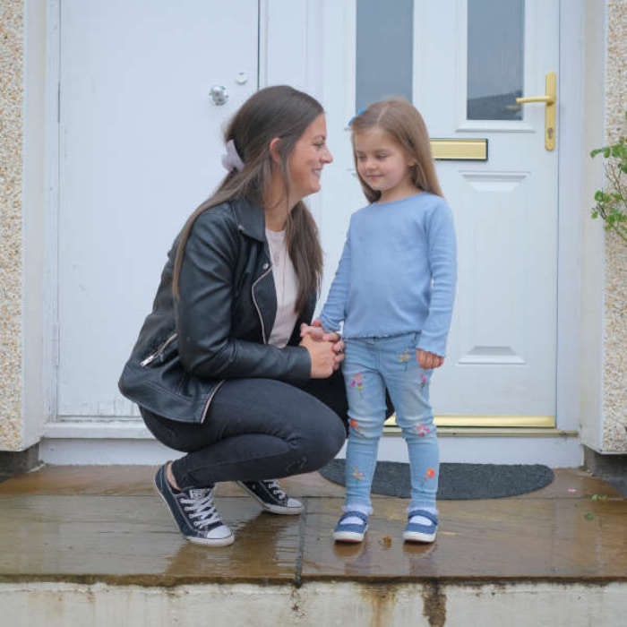 Image of a mum crouching down and smiling at her child in front of their front door.