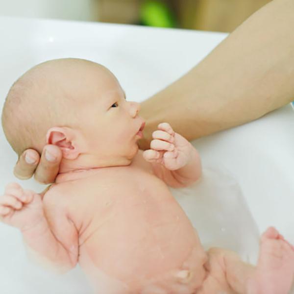 Image of an adult's hands supporting a baby in a baby bath.