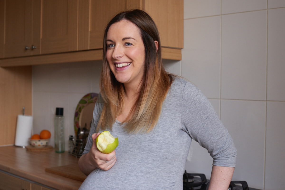 Image of an expecting mother holding an apple and smiling.