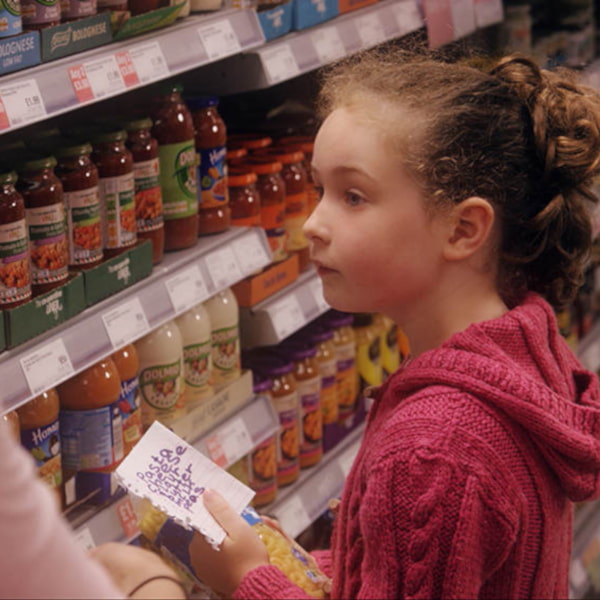 Image of a child in a supermarket with their mum, holding a shopping list and looking at the products on the shelves.