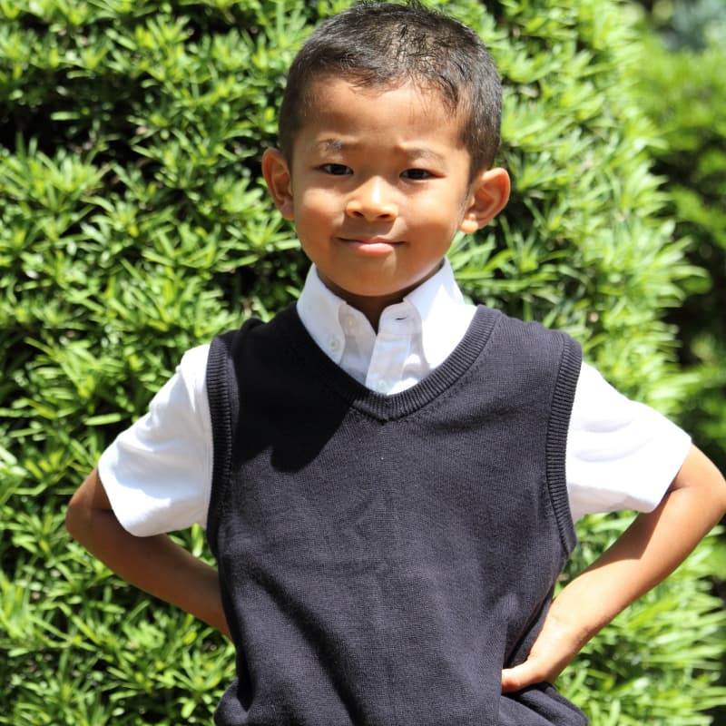 Image of a child standing in front of trees, smiling at the camera.