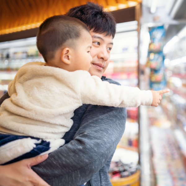 Image of a dad holding a toddler in a supermarket, the toddler is pointing at something on a shelf.