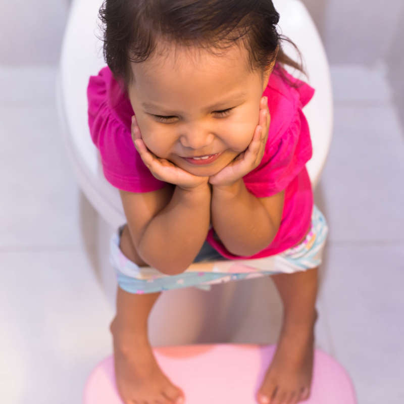 Image of a toddler smiling while sitting on a toilet.