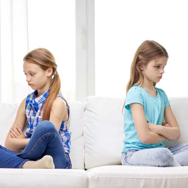 Two girls sitting back to back with their arms folded, looking cross