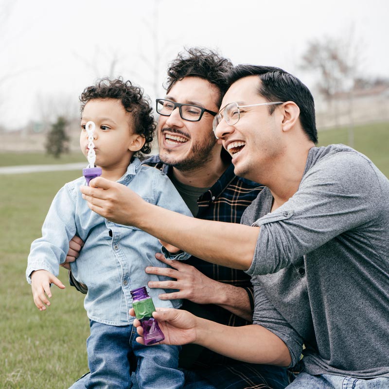 Dads and toddler blowing bubbles together in the park