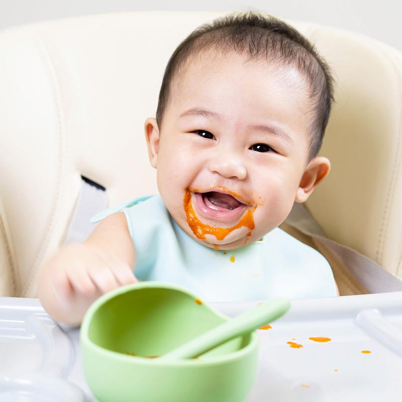 Baby in highchair with tomato soup round their mouth