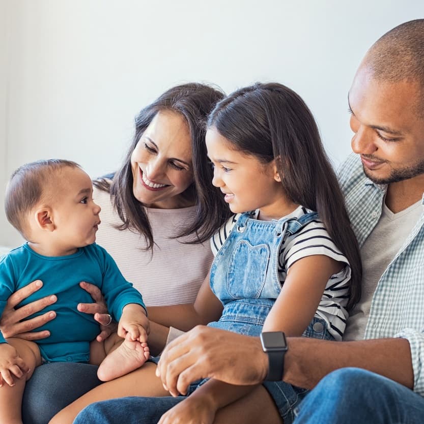 Mother, father, baby and young child sitting on a sofa