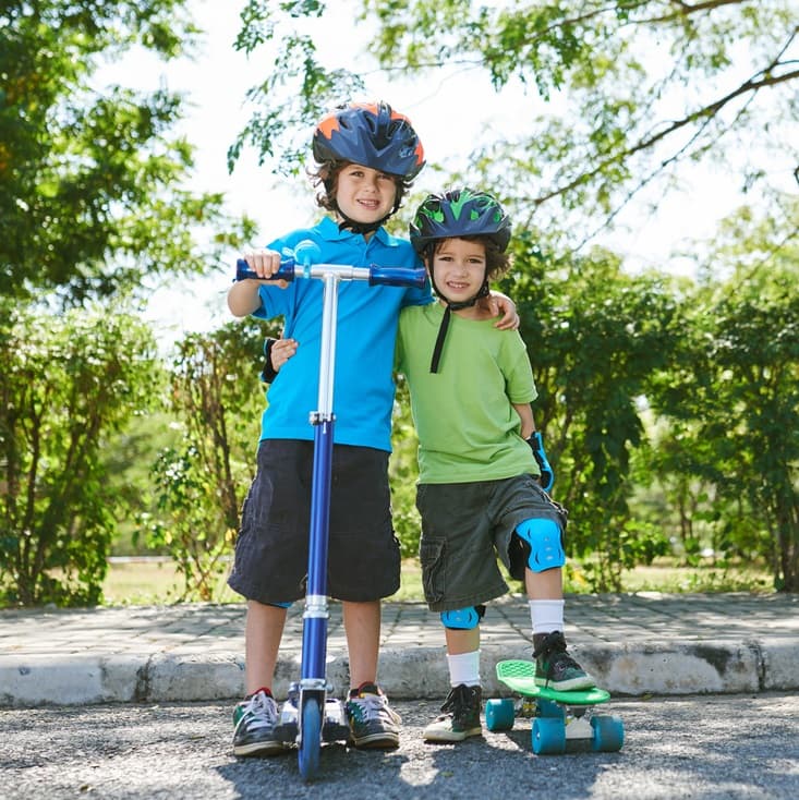 Two boys with a scooter and skateboard wearing helmets