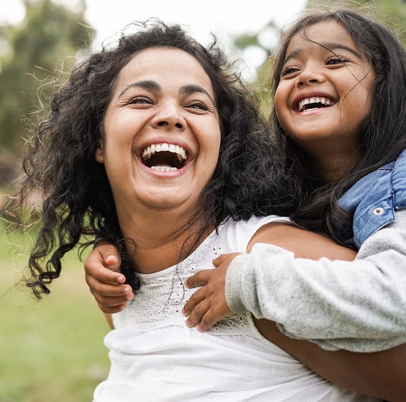 Mum and daughter outside in a park, both smiling and laughing
