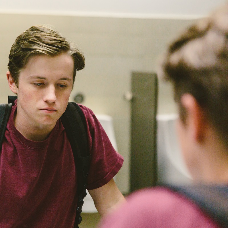 Teen boy looking in the mirror, looking sad