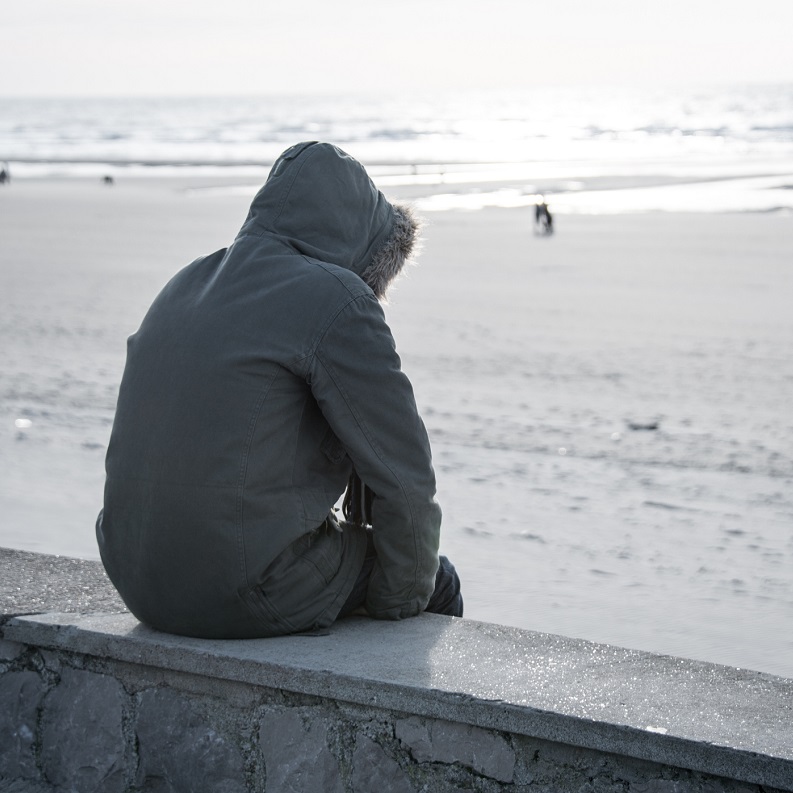 Sad teen wearing a hoodie, looking out to sea.