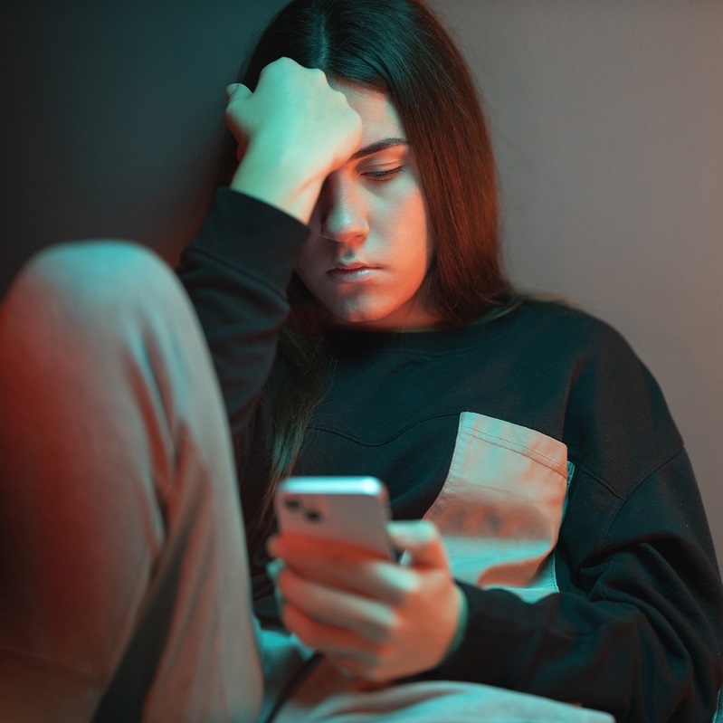 Sad teen girl looking at her mobile phone